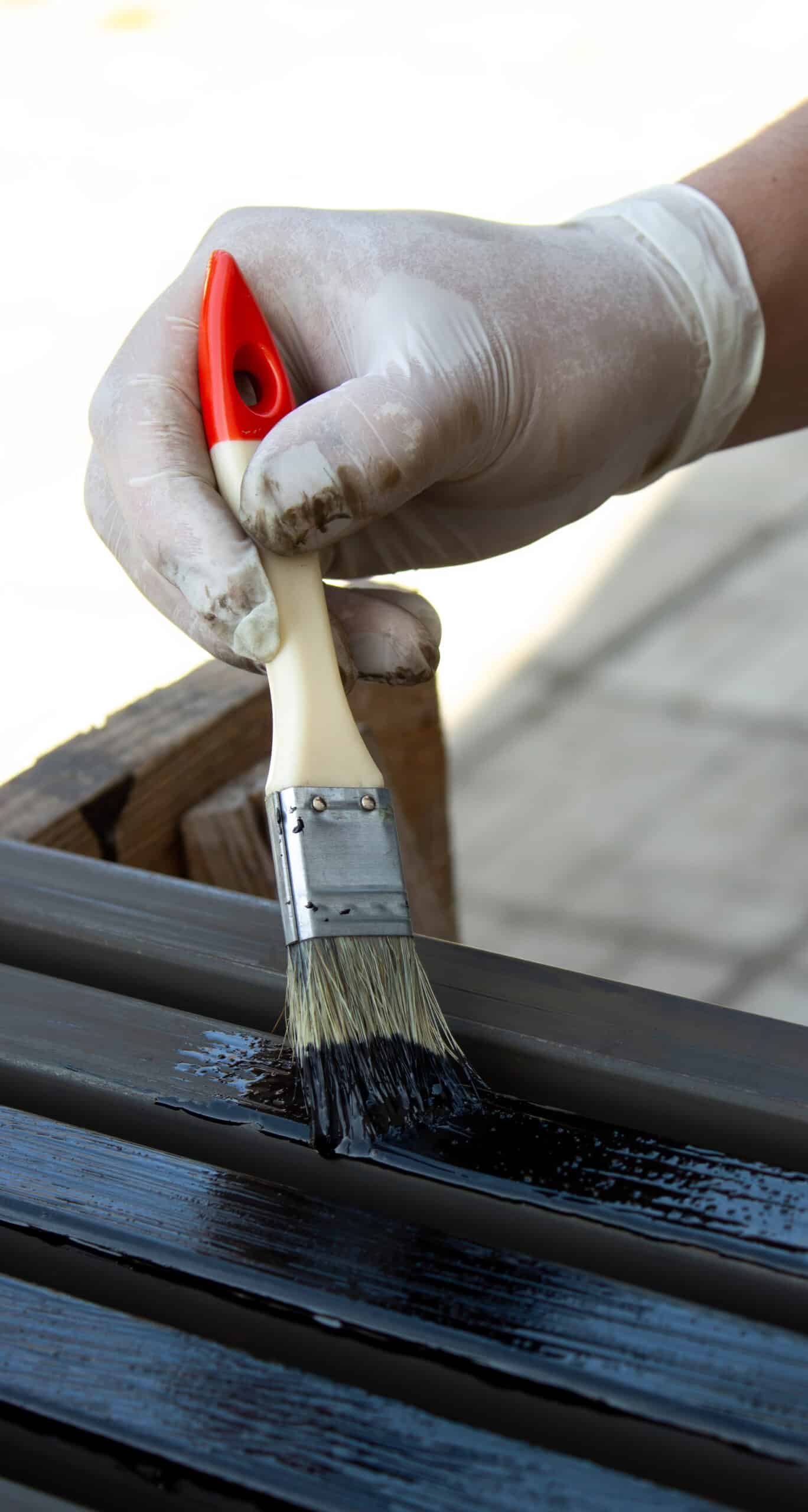 Application peinture noire bois et métal au pinceau Main gantée appliquant une peinture noire brillante sur des lattes métalliques avec un pinceau.