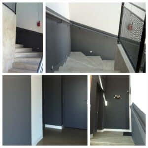 Escalier intérieur moderne avec murs gris anthracite, béton apparent et rampes métalliques. Portes sombres et éclairage discret.