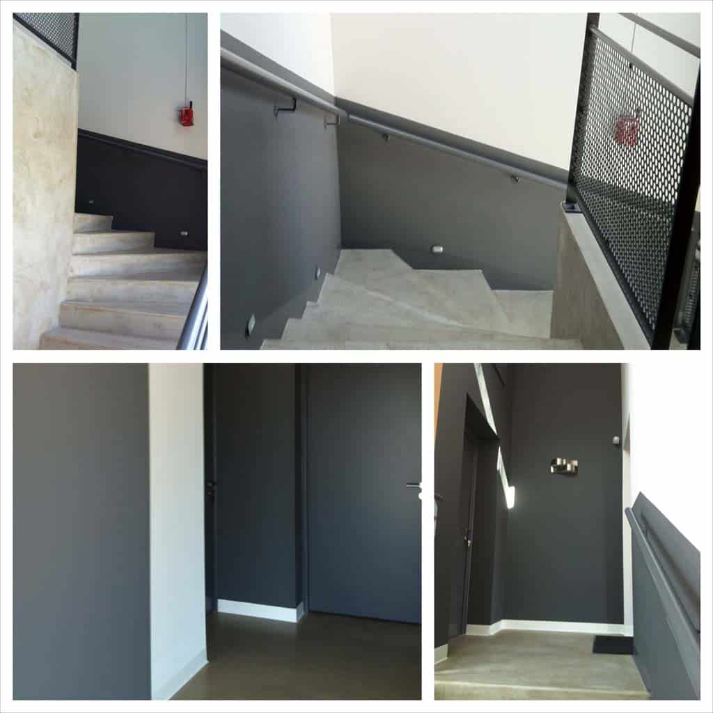 Escalier intérieur moderne avec murs gris anthracite, béton apparent et rampes métalliques. Portes sombres et éclairage discret.