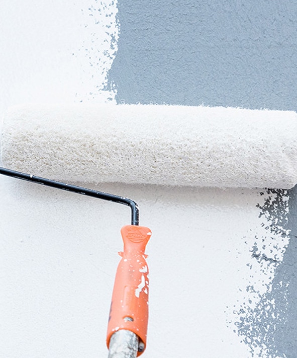 Application de peinture murale gris-bleu avec rouleau Rouleau à peinture blanc appliquant une peinture bleu-gris sur un mur blanc, poignée orange tachée de peinture.